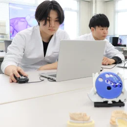 白衣姿の学生3人がノートPCで歯科のデジタルデータを確認している様子